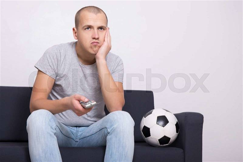 Bored soccer fan with ball watching game on tv at home, stock photo