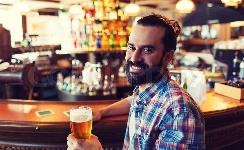 People, drinks, alcohol and leisure concept - happy young man drinking beer at bar or pub, stock photo