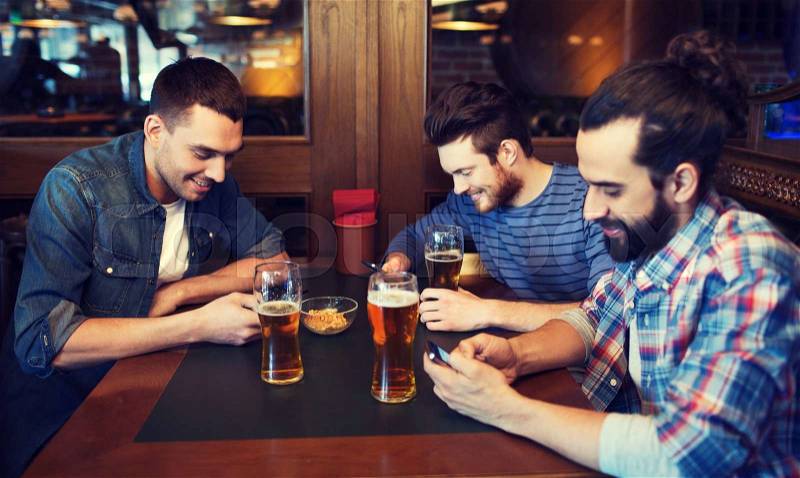 People, men, leisure, friendship and technology concept - male friends with smartphones drinking beer at bar or pub, stock photo