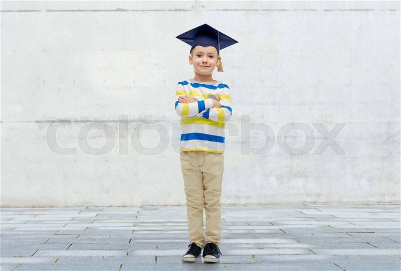 Childhood, school, education, learning and people concept - happy boy in bachelor hat or mortarboard over urban concrete background, stock photo