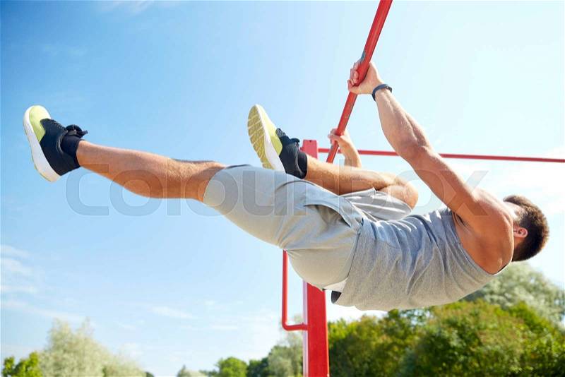 Fitness, sport, exercising, training and lifestyle concept - young man doing abdominal exercise on horizontal bar in summer park, stock photo