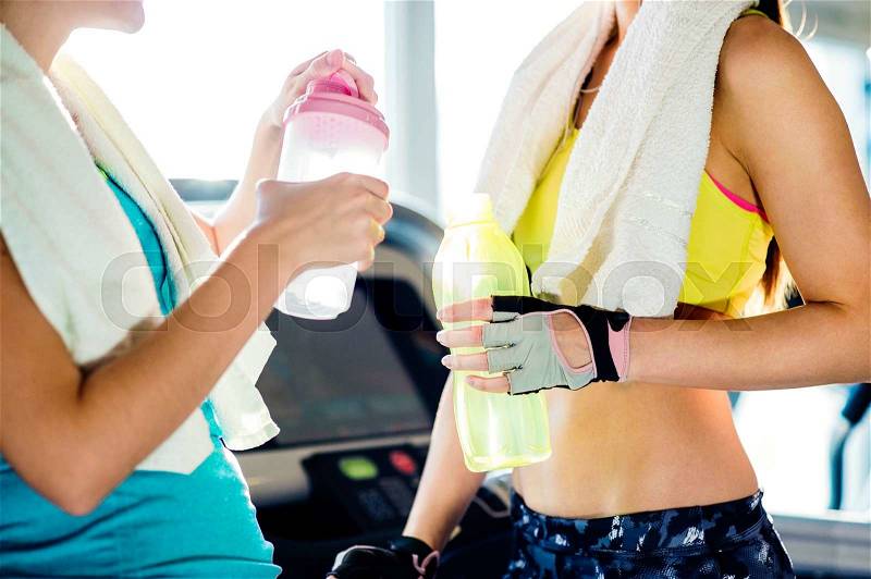 Two attractive fit women in a gym with water bottles and towels during a break, sunny day, stock photo