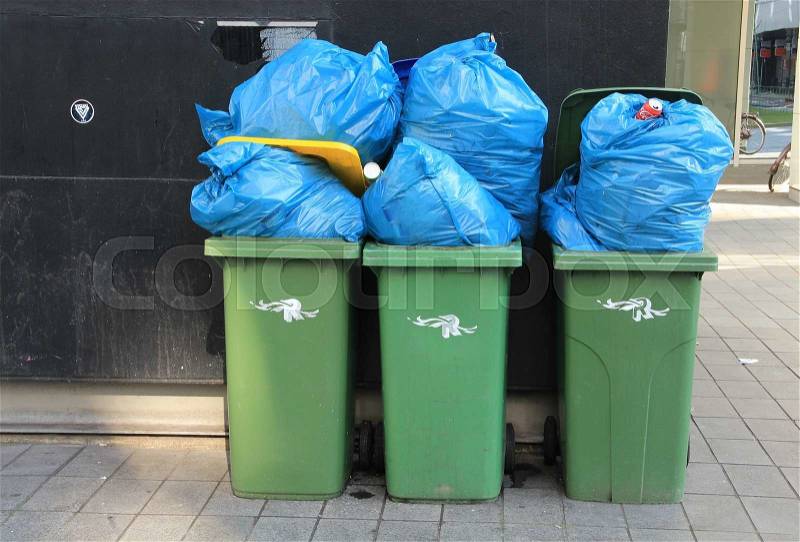 Streetscape with many green garbage cans are crammed with blue pastic waste bags in the residential area, stock photo