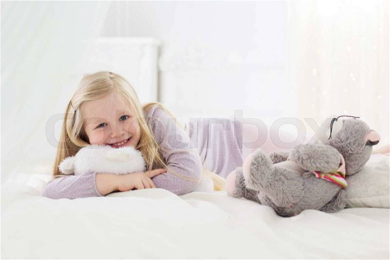 Happy pretty child girl is holding her soft toys in the bed, good morning, stock photo