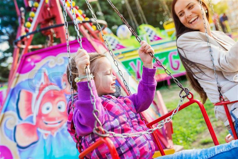 Cute little girl with her mother enjoying time at fun fair, chain swing ride, amusement park, stock photo