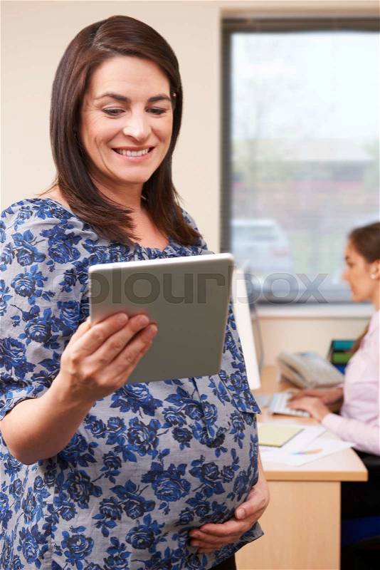 Pregnant Businesswoman Using Digital Tablet In Office, stock photo