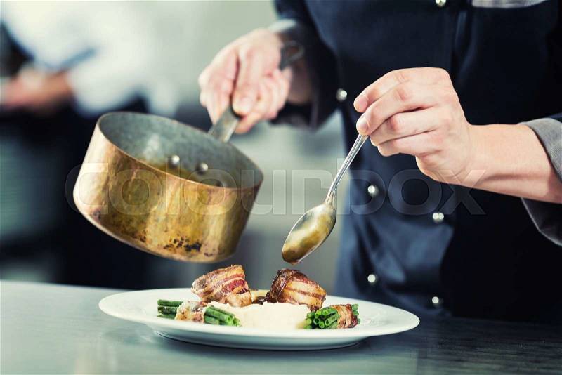 Chef pouring sauce on dish in restaurant kitchen, crop on hands, filtered image, stock photo