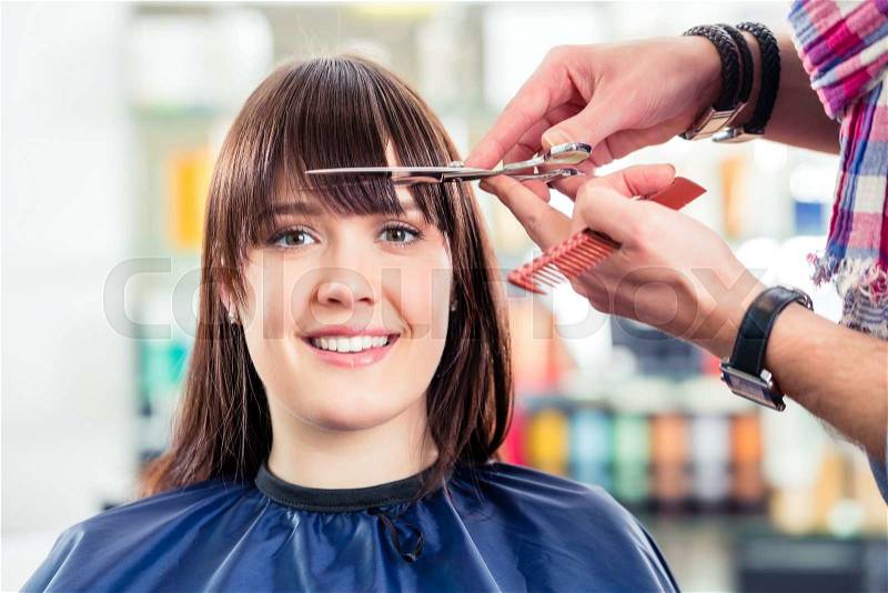 Hairdresser cutting woman bangs hair in shop, stock photo