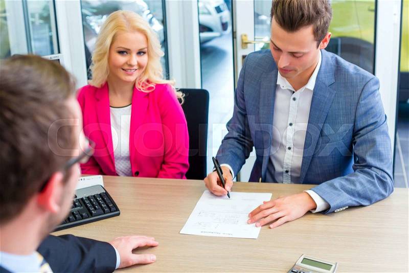 Couple buying car at dealership and signing sales contract with salesman, stock photo