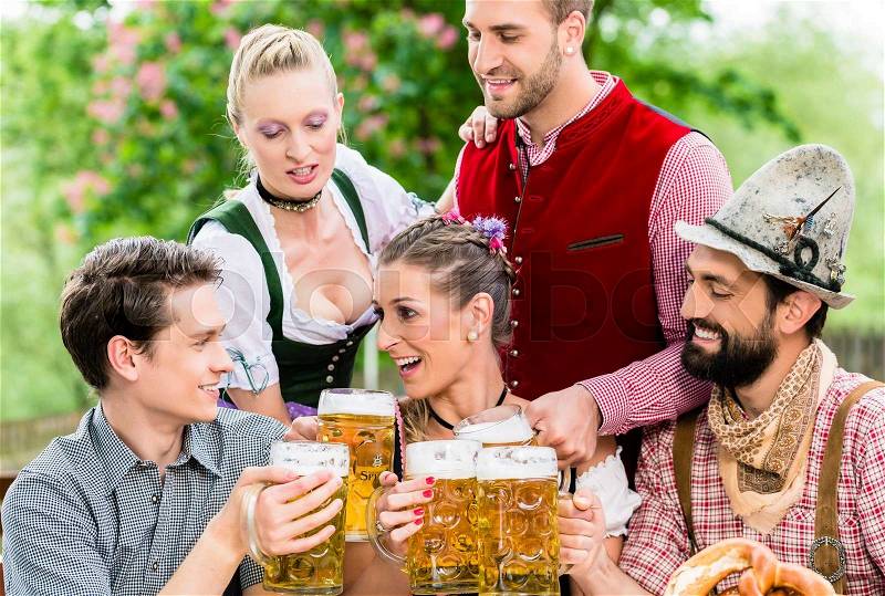 In Beer garden - friends in Tracht, Dirndl and Lederhosen drinking a fresh beer in Bavaria, Munich, Germany, stock photo