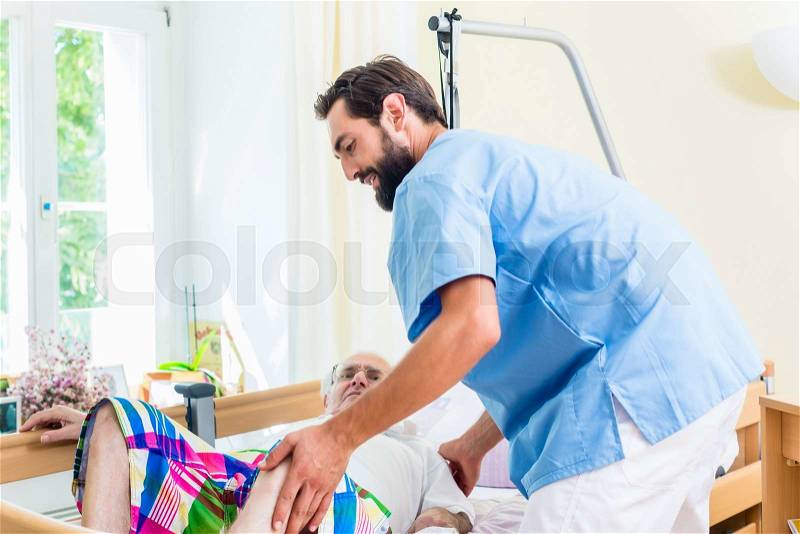 Elderly care nurse helping senior man from wheelchair to bed, stock photo