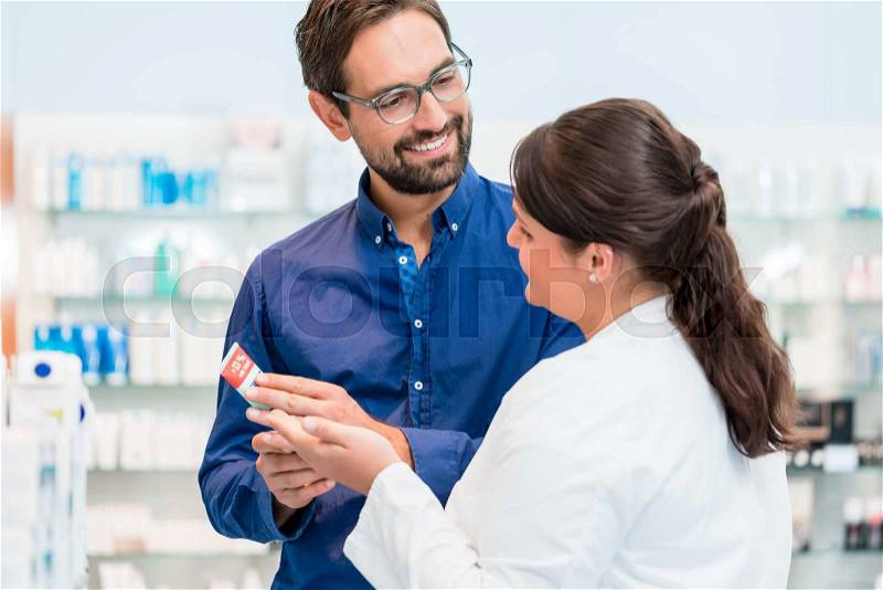 Pharmacist talking to customer in drug store, woman and man standing in front of shelves, stock photo