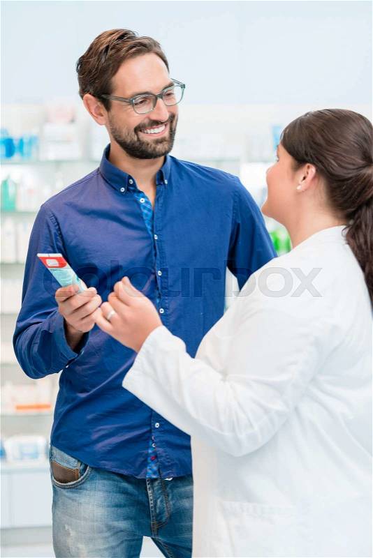Pharmacist talking to customer in drug store, woman and man standing in front of shelves, stock photo