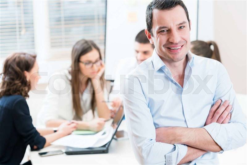 Boss in the office, his team having meeting in background, stock photo