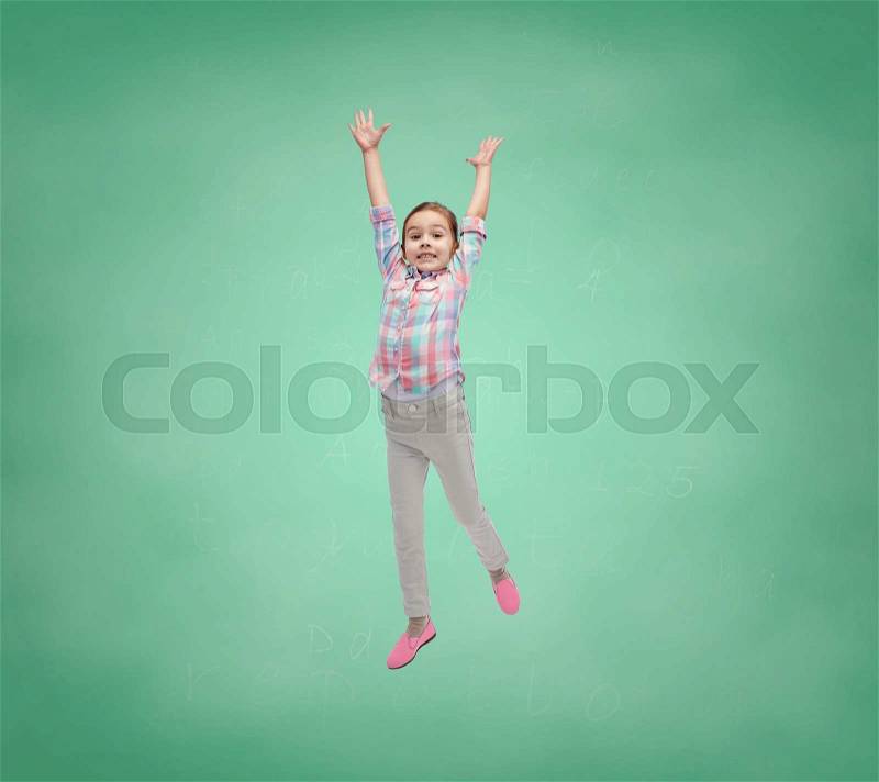 School, education, childhood, freedom and people concept - happy little girl jumping in air over green school chalk board background, stock photo