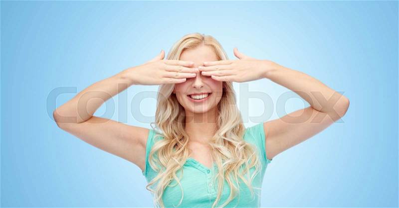Emotions, expressions and people concept - smiling young woman or teenage girl covering her eyes with palms over blue background, stock photo