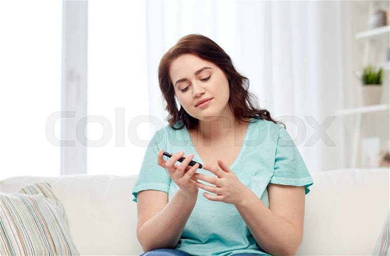 Medicine, diabetes, glycemia, health care and people concept - young plus size woman checking blood sugar level by glucometer at home, stock photo