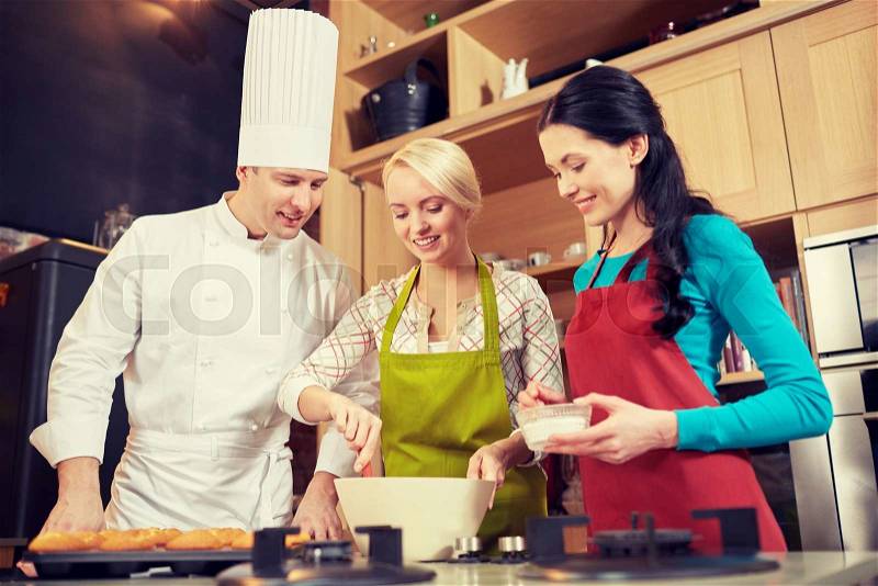 Cooking class, culinary, bakery, food and people concept - happy group of women and male chef cook baking muffins in kitchen, stock photo