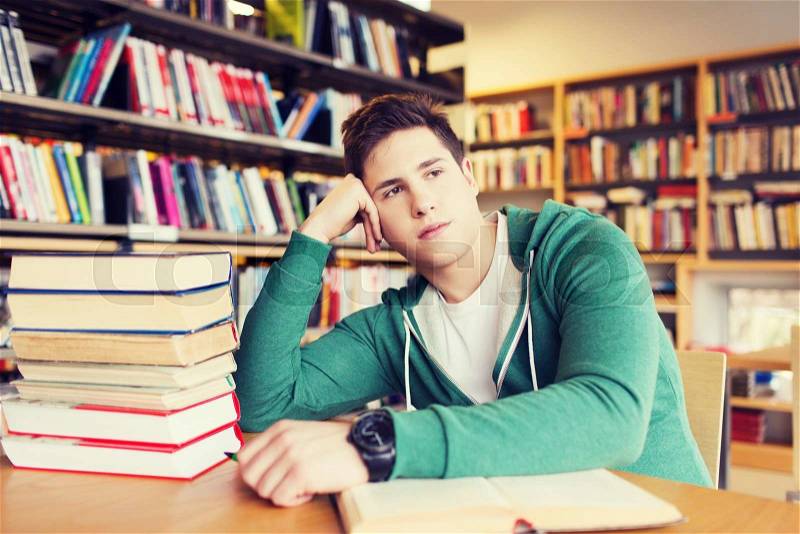 People, knowledge, education, literature and school concept - bored student or young man with books dreaming in library, stock photo