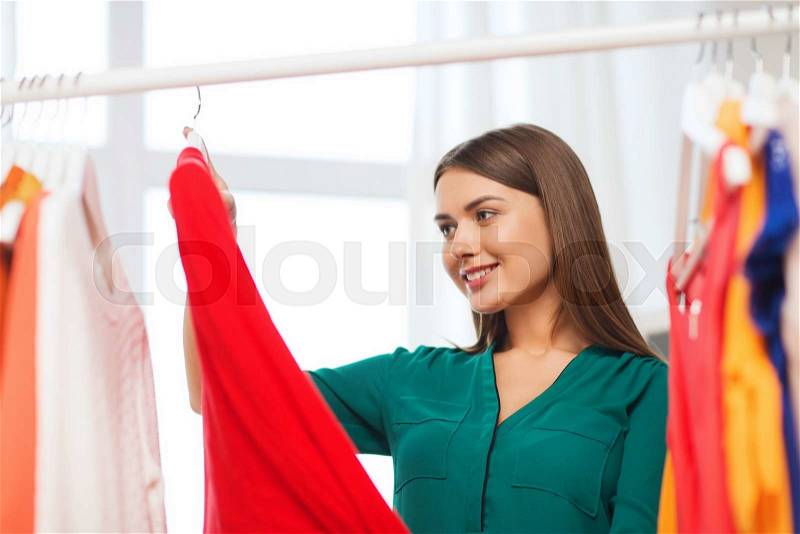 Clothing, fashion, style and people concept - happy woman choosing clothes at home wardrobe, stock photo