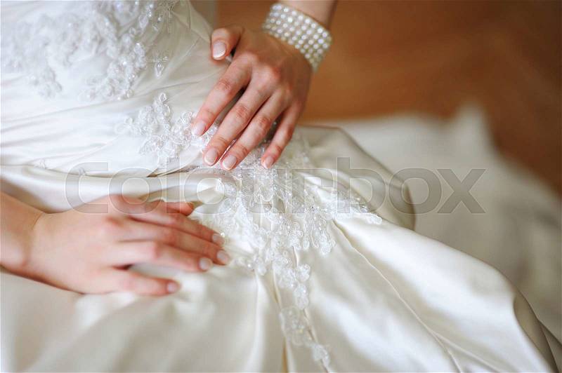 Elegant hands of the bride against background of dress, close-up, stock photo