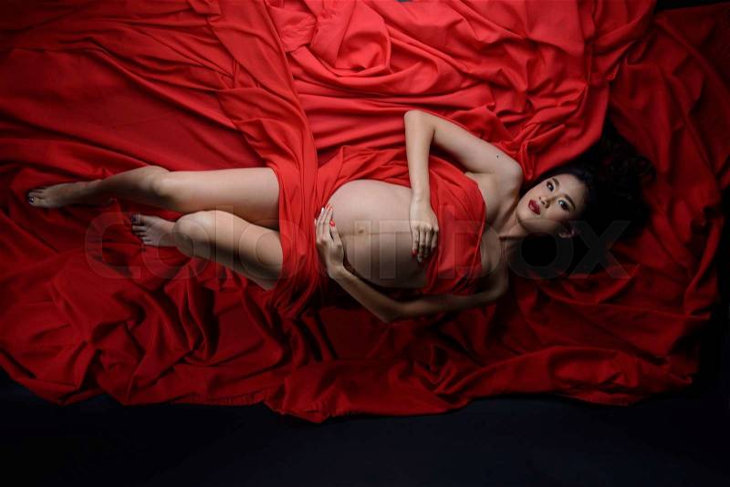 Glamour and style of beautiful young asian pregnant woman laying down on red fabric material, stock photo