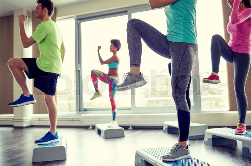 Fitness, sport, aerobics and people concept - group of smiling people working out and raising legs on step platforms in gym, stock photo