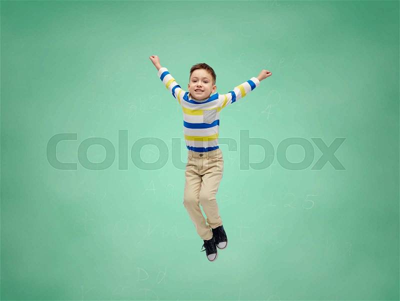 School, education, childhood, freedom and people concept - happy little boy jumping in air over green school chalk board background, stock photo