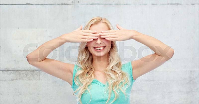 Emotions, expressions and people concept - smiling young woman or teenage girl covering her eyes with palms over gray concrete wall background, stock photo