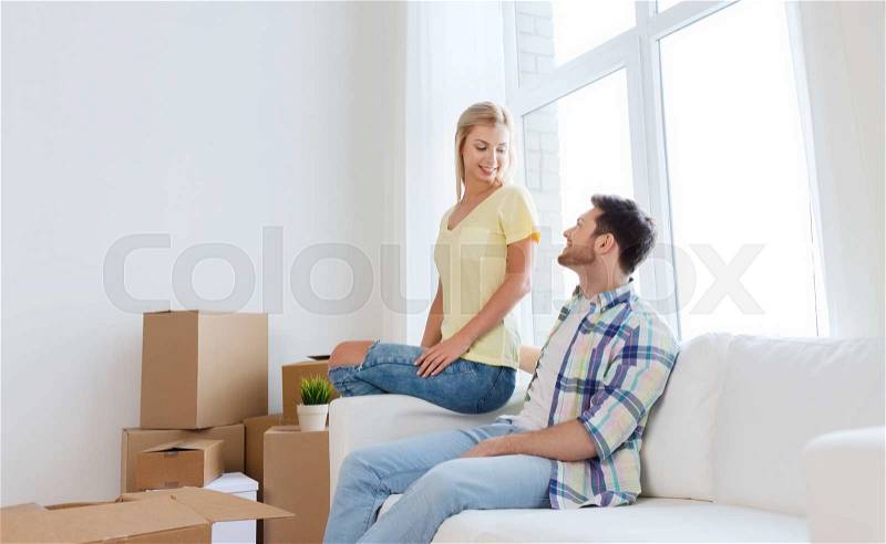 Moving, people, repair and real estate concept - happy couple with big cardboard boxes on sofa at new home, stock photo