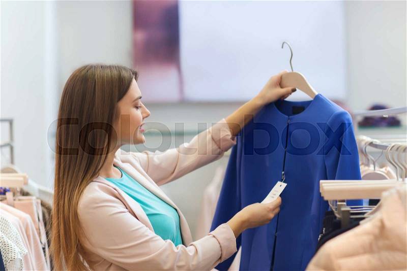 Sale, shopping, fashion, style and people concept - happy young woman choosing clothes in mall or clothing store, stock photo