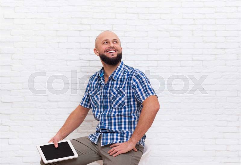Casual Bearded Man Stand Holding Tablet Computer Look Up To Copy Space Over White Brick Wall, stock photo