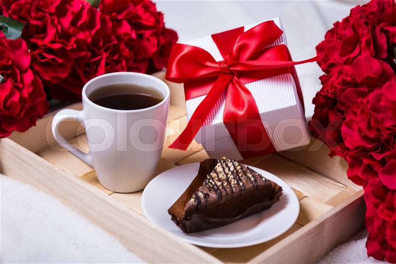 Holiday concept - close up of breakfast with chocolate cake, tea and little gift on wooden tray, stock photo