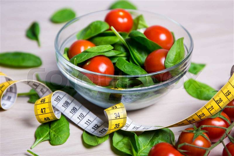 Diet and weight loss concept - salad with spinach and tomatoes and measure tape on wooden table background, stock photo