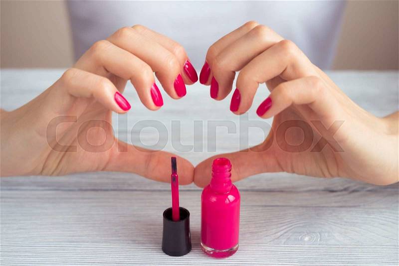 Female hands with pink manicure and the open bottle of varnish on the table, stock photo