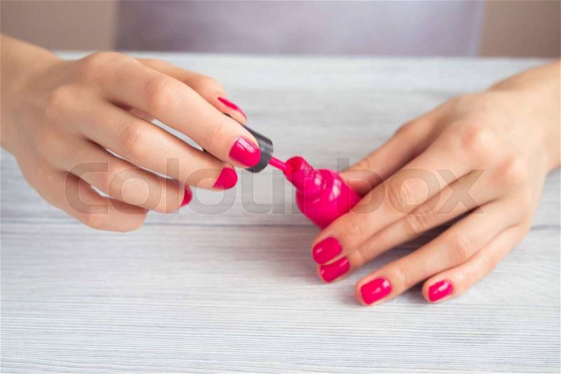 Women\'s hands with a red manicure open a bottle of varnish, stock photo