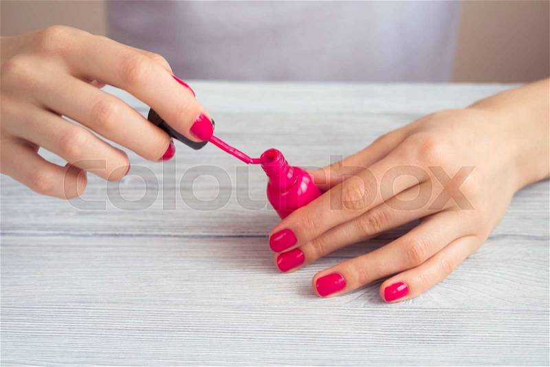 Female hands with pink manicure holding an open bottle of lacquer, stock photo