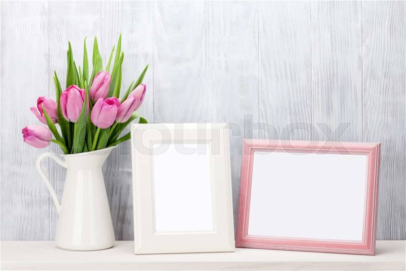 Fresh pink tulip flowers bouquet and blank photo frames with copy space on shelf in front of wooden wall, stock photo