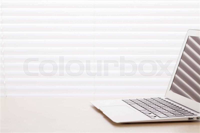 Office workplace with laptop on wood desk table in front of window with blinds, stock photo