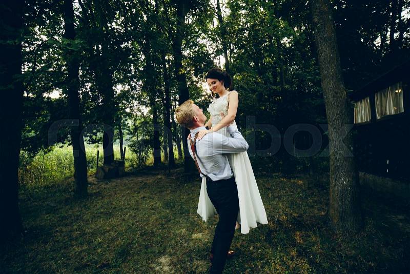 Groom lifted bride in his arms in the park, stock photo