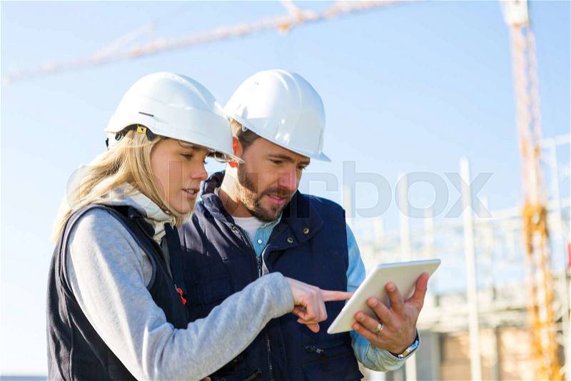 View of Two workers working outside with a tablet on a construction site, stock photo