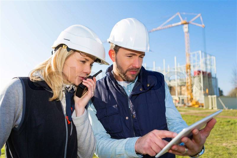 View of Two workers working outside with a tablet on a construction site, stock photo