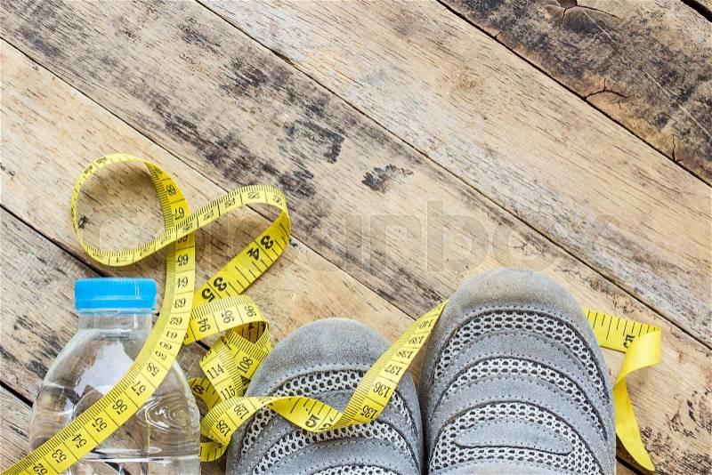 Yellow measuring tape, sport shoes and bottle water on wooden table - fitness concept, stock photo
