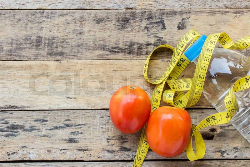 Yellow measuring tape, tometos and bottle water on wooden table - fitness concept, stock photo