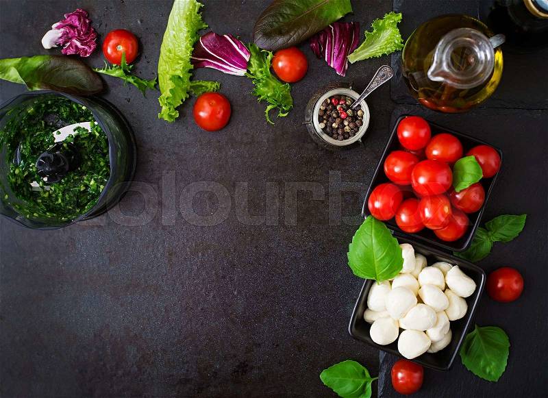 Ingredients Caprese salad tomato and mozzarella with basil and herbs oon black background. Top view, stock photo