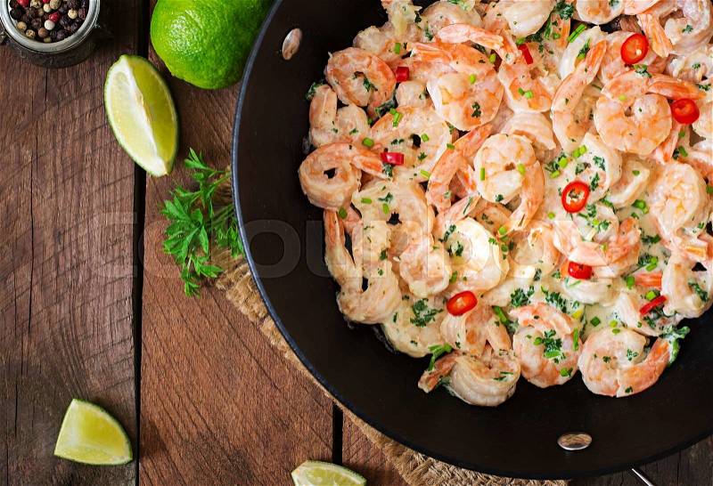 Shrimp in a creamy garlic sauce with parsley and lime in a frying pan. Top view, stock photo