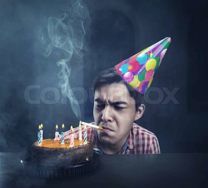 Sad birthday boy smoking in an abandoned room with cake, stock photo
