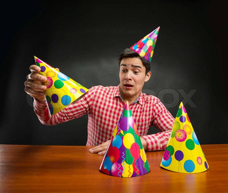Young man playing with Birthday hats at the table, stock photo