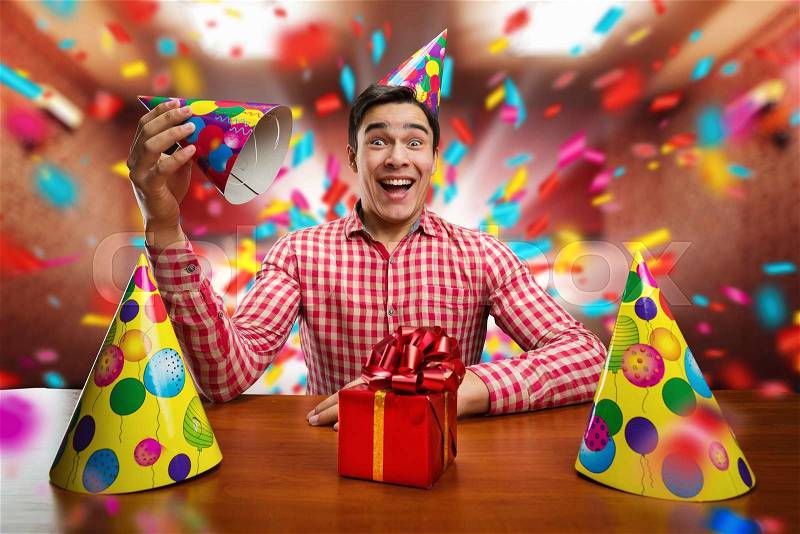 Young smiling man playing with Birthday hats at the table, stock photo