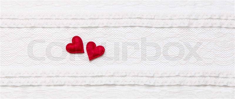 Two red hearts on white lace fabric, border design element, stock photo
